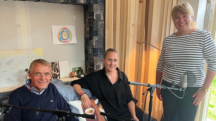 Bilde av programlederne og gjesten som sitter i studio med mikrofonen foran seg.