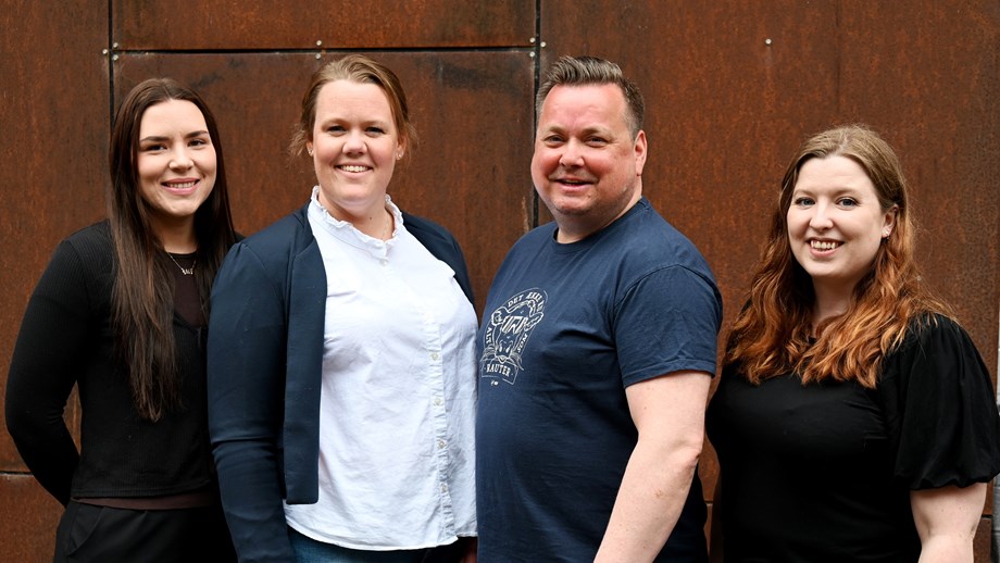 Alle fire i kundesenteret stå oppstilt utendørs mot en vegg. Alle smiler og ser mot fotografen.