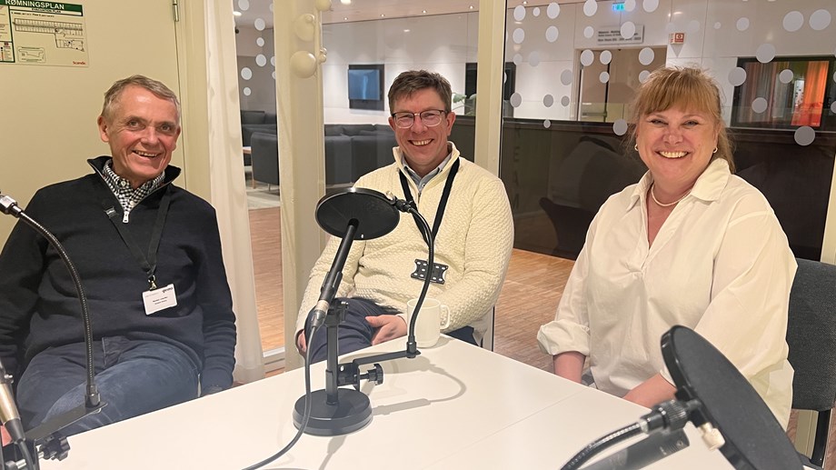 Programlederne sitter ved et bord sammen med gjesten som sitter i midten.