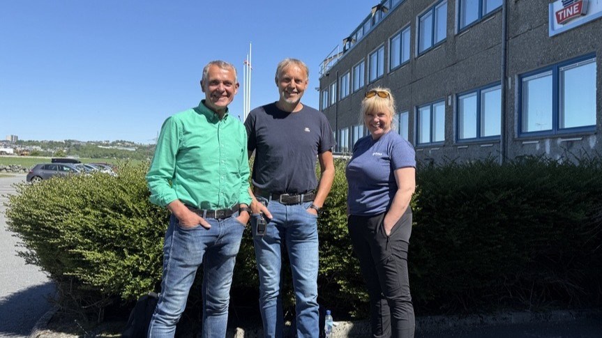 Programlederne og gjesten står oppstilt ute i solen og smiler mot kamera.