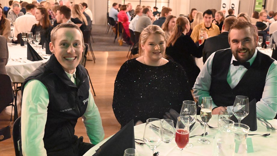 Vegard med Geno-vest sitter ved et bord sammen med Beate og Olav. Alle ser mot kamera og smiler. I bakgrunnen vises flere bord med festdeltakere.