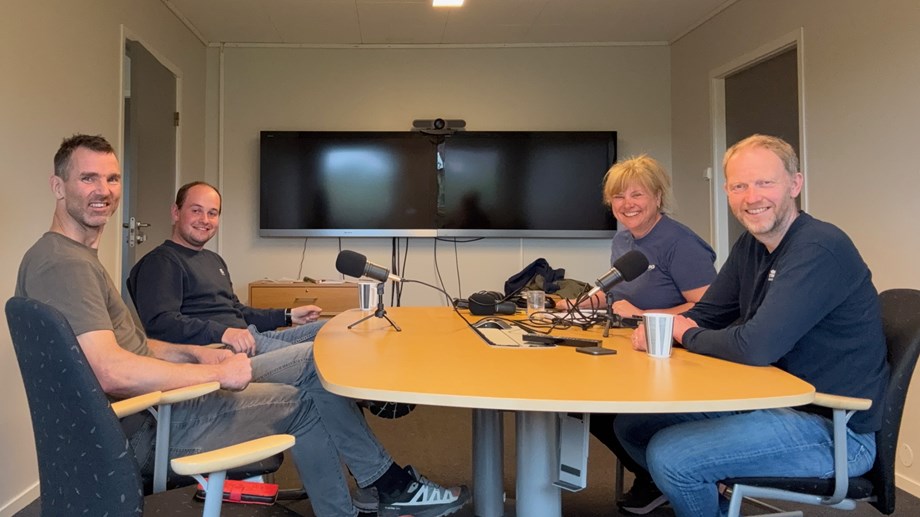 Gjester og programledere sitter rundt et bord med mikrofoner på bordet.