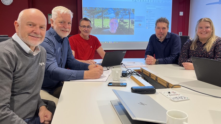 Personene i hovedkomitéen sitter rundt et bord og ser mot kamera. En av deltakerne er med via skjerm som vises i bakgrunnen.