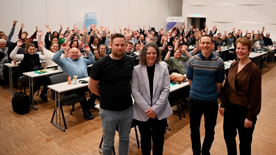 Samtlige årsmøteutsendinger sitter i møtesalen og rekker hendene i været. Foran forsamlingen står møtelederne, styreleder og administrerende direktør.