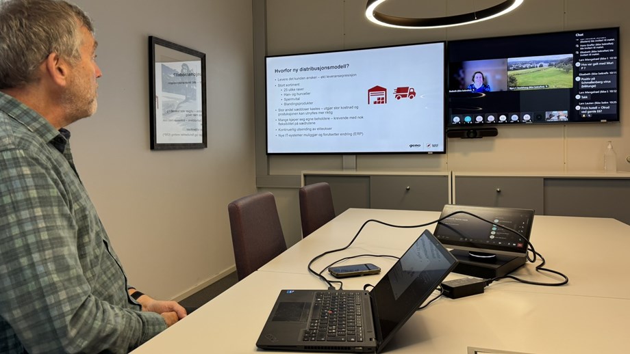 Hans Storlien sitte ved møtebordet og ser mot skjermen på veggen. Skjermene viser presentasjonen og møtedeltakerne.