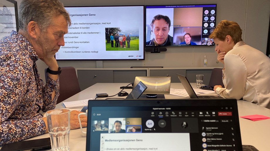 Hans og Kristin sitte ved et møtebord med pc foran seg. På skjermen vises plansje og deltaker i møtet.