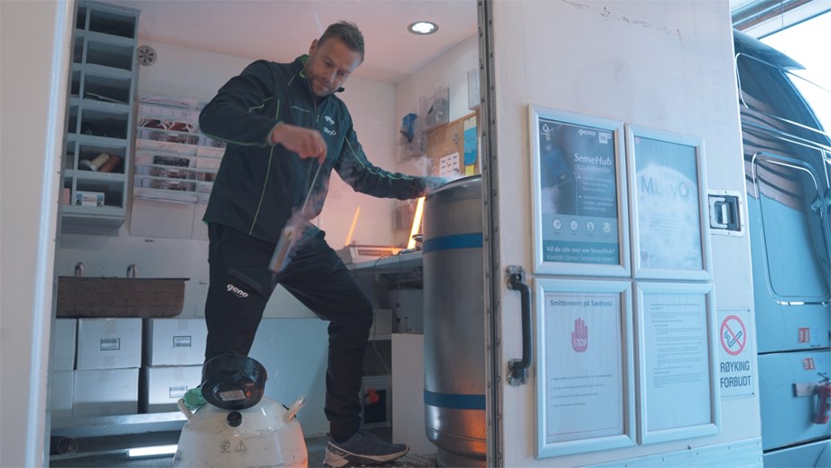 En mann i Genos profilkær står i åpningen på sædrutebilen og løfter en dublett med sæddoser fra en tank i bilen til en beholder. 
