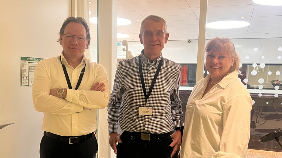 Programlederne står sammen med gjesten i Genopoddens studio. De står oppstilt og ser mot fotografen.